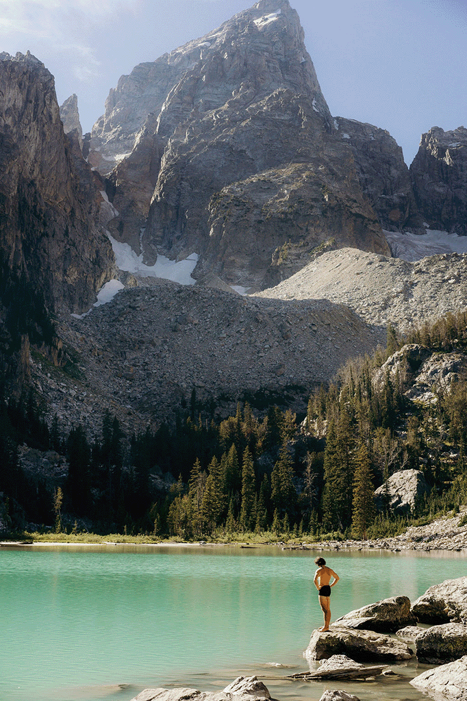 man jumping into a mountain lake with mountains and pines in the background