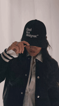 Sandy Chang in varsity jacket and "God is a designer" hat, showcasing creative confidence and bold brand identity.