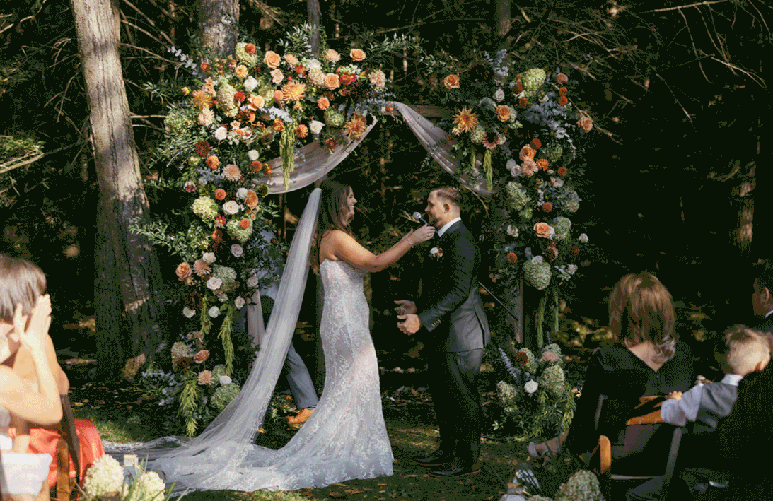 bride and groom kissing under flower arch during their wedding ceremony