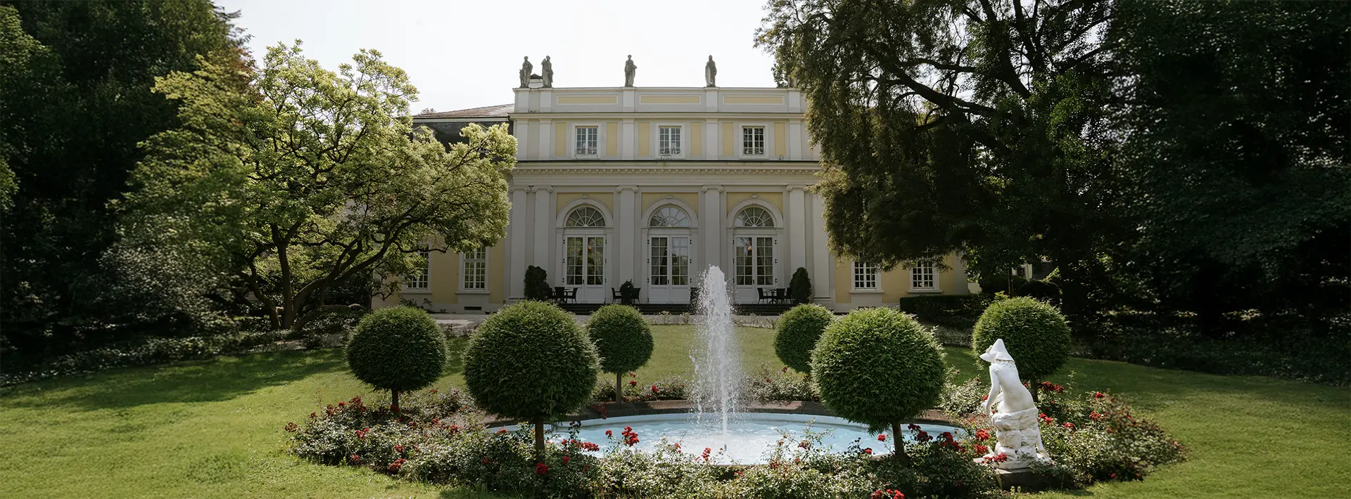 Vor der klassizistischen Villa sprudelt ein Brunnen, umrahmt von Rosen und Buchskugeln – perfekte Kulisse für natürliche Hochzeitsfotografie und hochzeitsbilder draußen