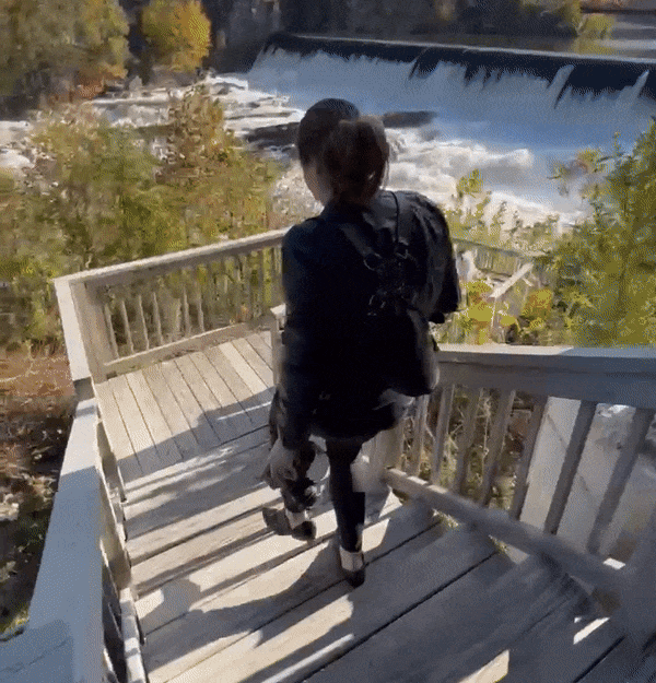A gif of Brea Warren taking a photo of a couple walking down stairs towards waterfall