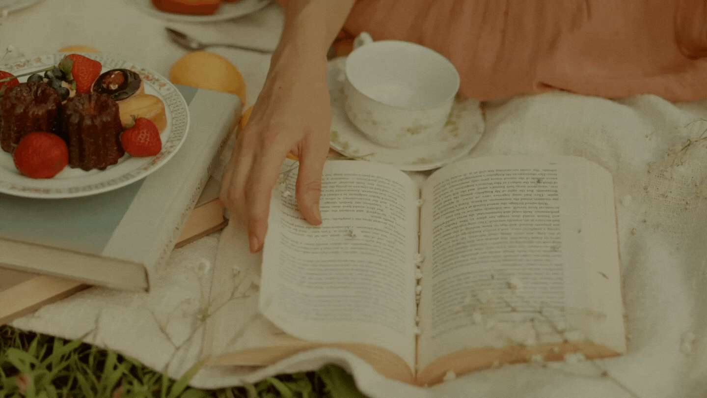 Woman's hand flipping through pages of an old book on a picnic blanket in the park
