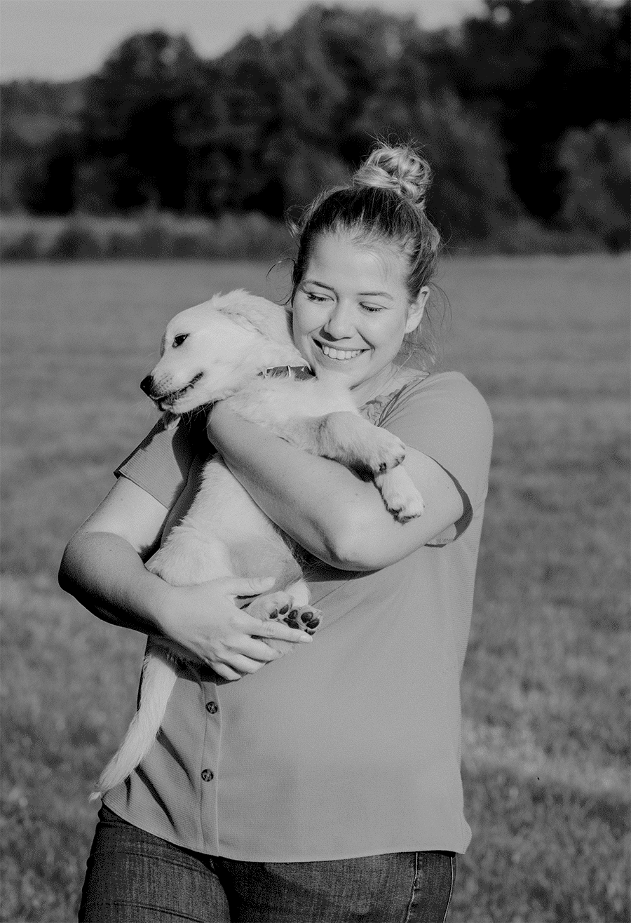 Julia Weinberger mit ihrem Hundewelpen Klea auf dem Arm in schwarz-weiß auf einer Wiese.