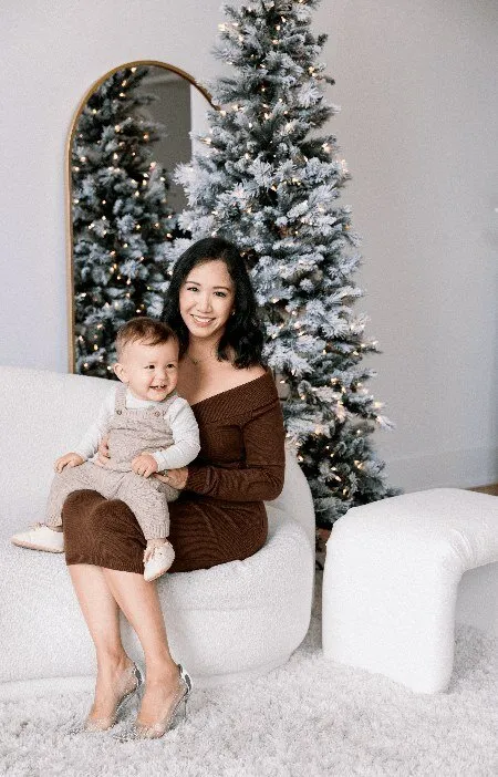Mom holding her baby beside a flocked tree
